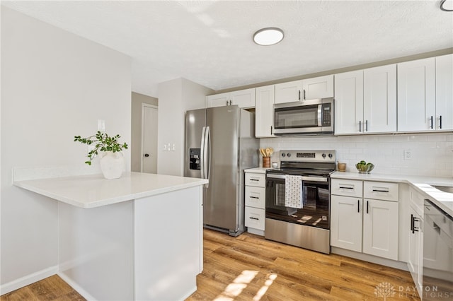 kitchen with backsplash, appliances with stainless steel finishes, light countertops, and light wood-type flooring