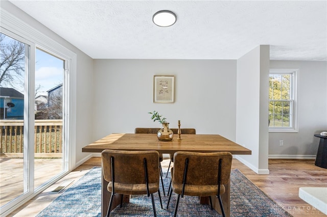 dining area featuring light wood-style flooring, baseboards, and a textured ceiling