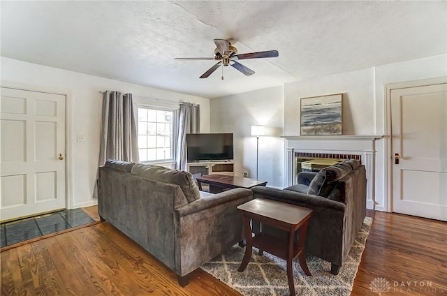 living area featuring a ceiling fan, a fireplace, dark wood-style flooring, and a textured ceiling