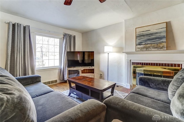 living room featuring visible vents, a ceiling fan, wood finished floors, baseboards, and a brick fireplace