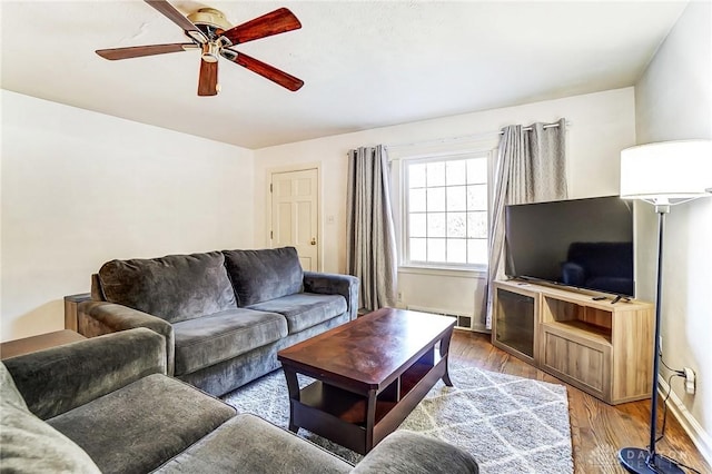 living area with a baseboard heating unit, wood finished floors, baseboards, and ceiling fan