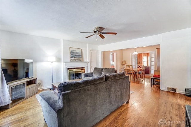 living area with visible vents, light wood-style flooring, baseboards, a brick fireplace, and ceiling fan