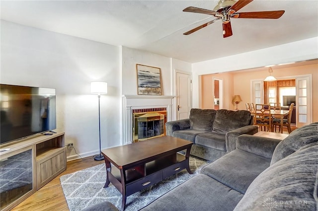 living room with a brick fireplace, light wood finished floors, and ceiling fan