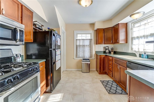 kitchen with light tile patterned floors, baseboards, a sink, decorative backsplash, and appliances with stainless steel finishes