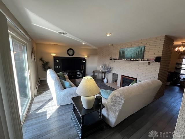 living area featuring an inviting chandelier, a brick fireplace, wood finished floors, and brick wall