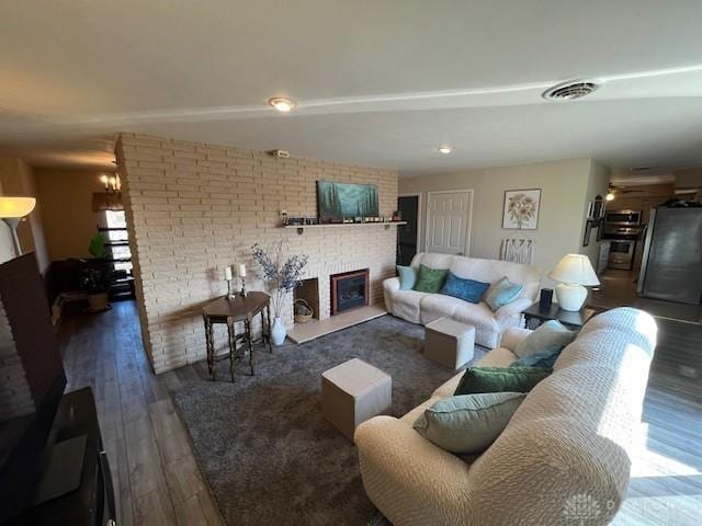 living room with visible vents, a brick fireplace, brick wall, and wood finished floors