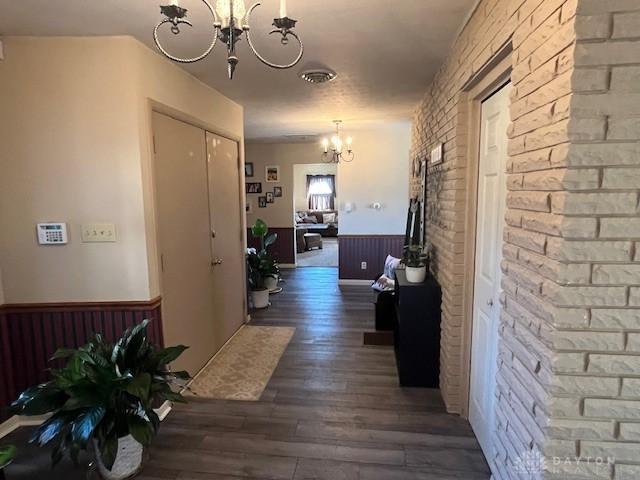 corridor with dark wood-style floors, a wainscoted wall, brick wall, wood walls, and a chandelier