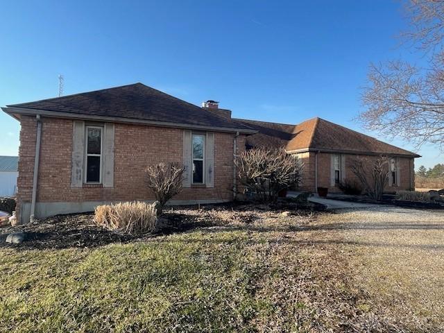 exterior space featuring a lawn, brick siding, roof with shingles, and a chimney