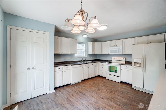 kitchen featuring a sink, dark countertops, dark wood finished floors, white appliances, and a chandelier