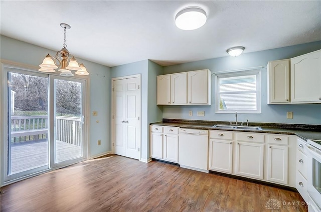 kitchen featuring light wood finished floors, white dishwasher, a sink, dark countertops, and a notable chandelier