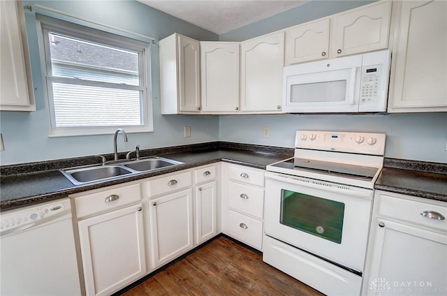 kitchen featuring dark countertops, white cabinets, white appliances, and a sink