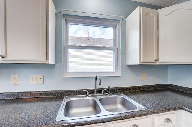 kitchen with dark countertops, white cabinetry, and a sink