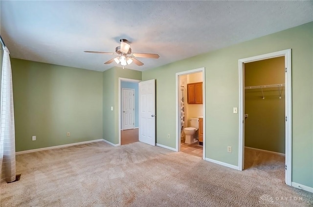 unfurnished bedroom with a spacious closet, ensuite bath, baseboards, and carpet floors