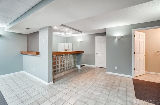 interior space with visible vents, baseboards, white fridge with ice dispenser, and a bar