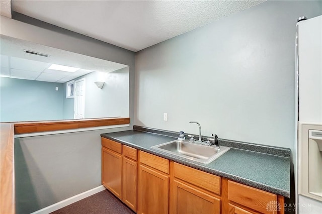 kitchen featuring visible vents, a sink, a paneled ceiling, dark countertops, and dark carpet