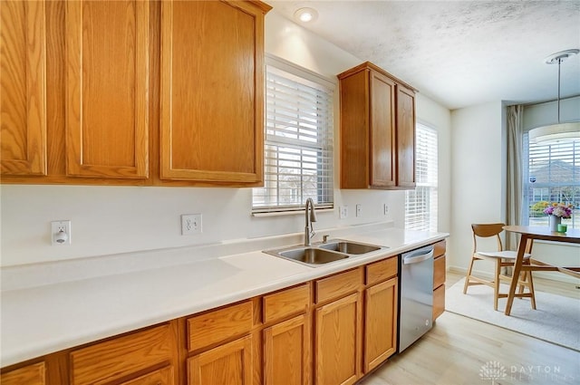 kitchen featuring stainless steel dishwasher, light countertops, brown cabinetry, and a sink