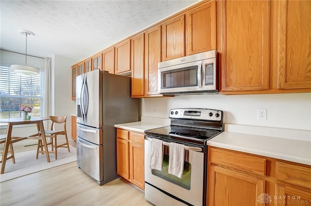 kitchen with light wood-style flooring, hanging light fixtures, light countertops, appliances with stainless steel finishes, and a textured ceiling