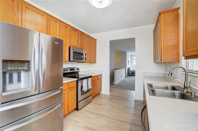 kitchen featuring a sink, light countertops, appliances with stainless steel finishes, a textured ceiling, and light wood-type flooring