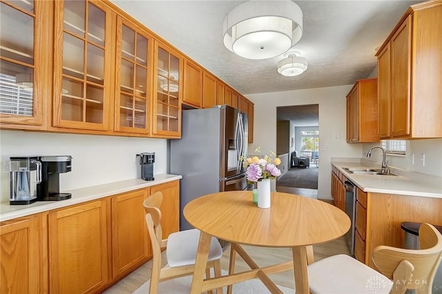 kitchen with light countertops, glass insert cabinets, brown cabinetry, and a sink