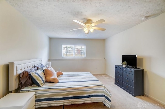 bedroom featuring baseboards, light colored carpet, a textured ceiling, and a ceiling fan