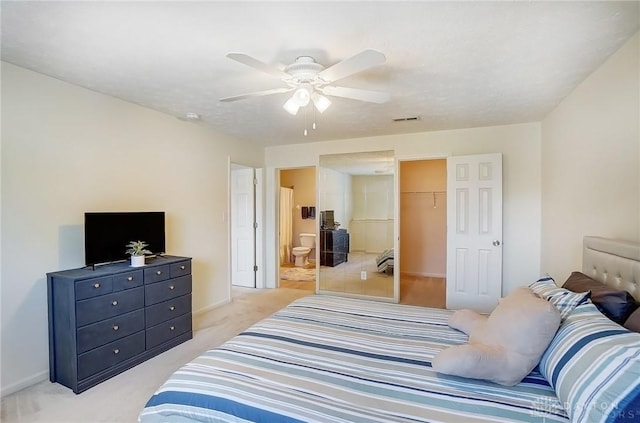 bedroom with a spacious closet, visible vents, ceiling fan, light colored carpet, and ensuite bathroom