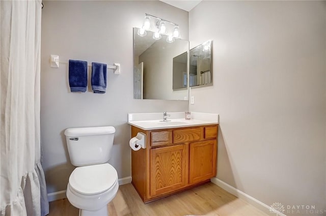 bathroom with toilet, vanity, baseboards, and wood finished floors