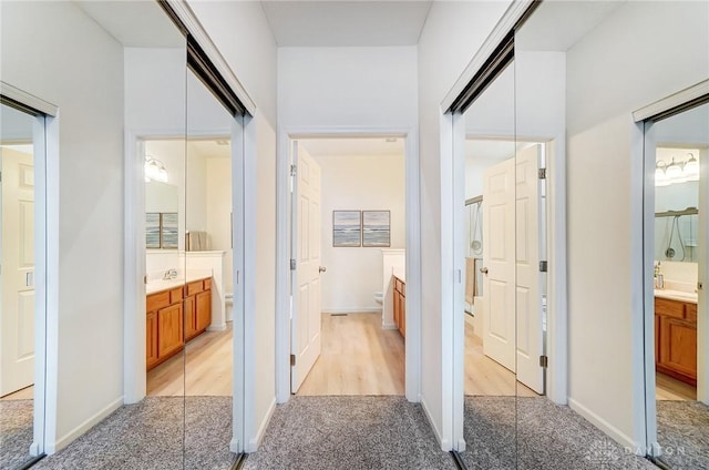 corridor featuring light colored carpet and baseboards