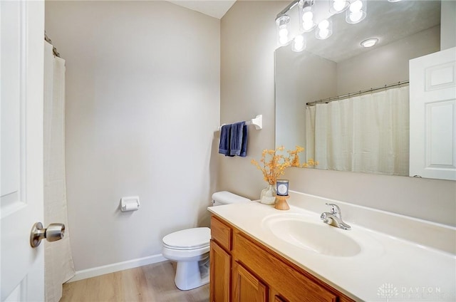 bathroom with toilet, vanity, baseboards, and wood finished floors