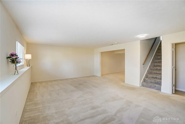 unfurnished room featuring light colored carpet, stairs, and baseboards