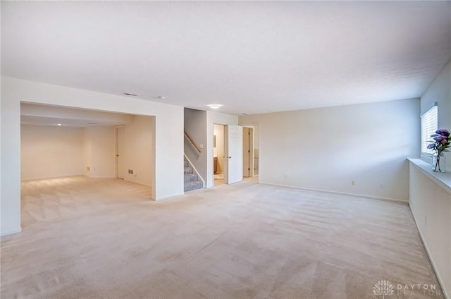 spare room with stairs, light colored carpet, and baseboards