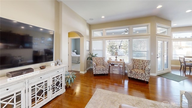 living area featuring a ceiling fan, wood finished floors, arched walkways, and a healthy amount of sunlight