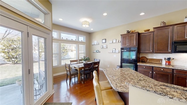 kitchen with light stone counters, black appliances, wood finished floors, and recessed lighting