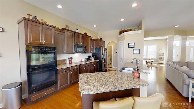 kitchen featuring a sink, light wood-style flooring, black appliances, and open floor plan