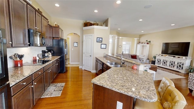 kitchen featuring arched walkways, a sink, black appliances, a kitchen breakfast bar, and open floor plan