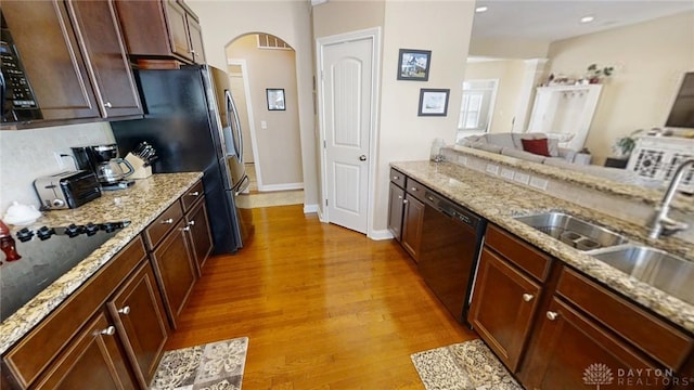 kitchen featuring light wood finished floors, arched walkways, a sink, black appliances, and open floor plan