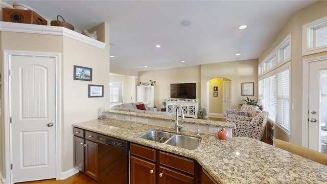 kitchen with light stone countertops, open floor plan, dishwasher, arched walkways, and a sink