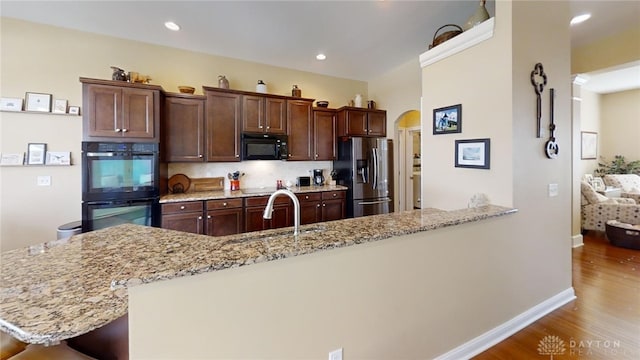 kitchen with light stone countertops, wood finished floors, arched walkways, black appliances, and a sink