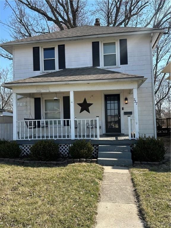 american foursquare style home featuring a front yard, covered porch, and a chimney