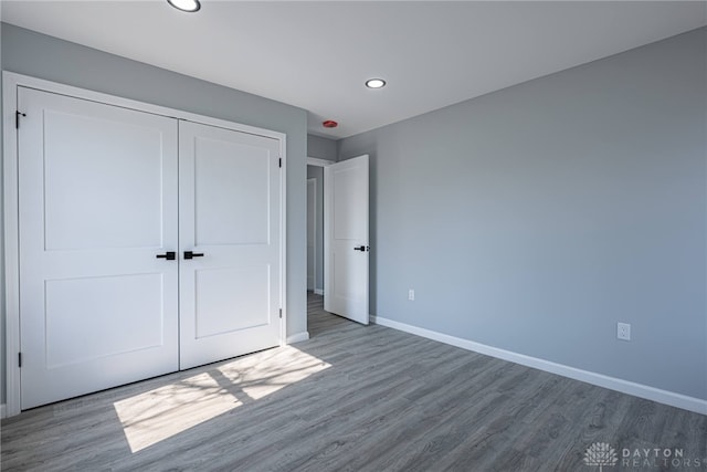 unfurnished bedroom with recessed lighting, wood finished floors, baseboards, and a closet