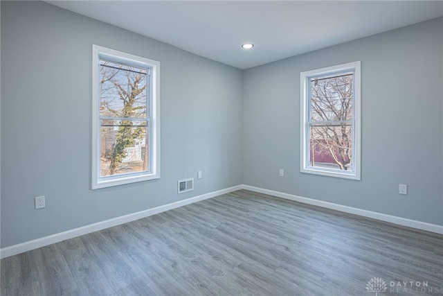 unfurnished room with visible vents, plenty of natural light, baseboards, and wood finished floors