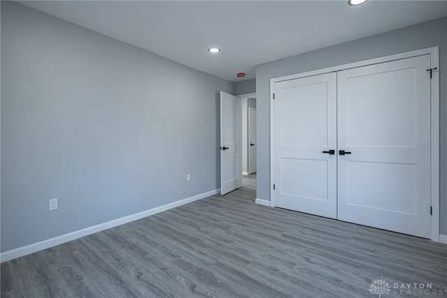 unfurnished bedroom with recessed lighting, a closet, baseboards, and wood finished floors