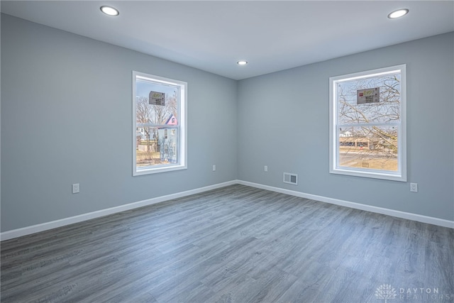 empty room with visible vents, a healthy amount of sunlight, baseboards, and wood finished floors