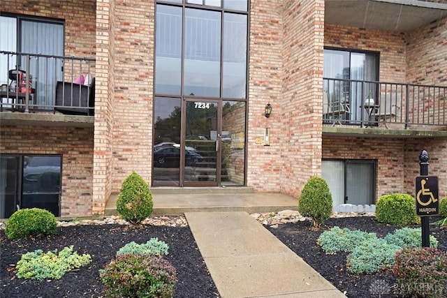 view of exterior entry featuring a balcony and brick siding