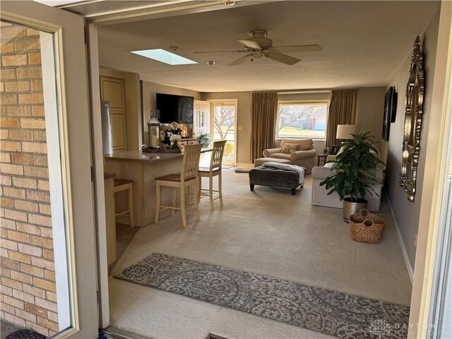 carpeted living area featuring a skylight, baseboards, and ceiling fan