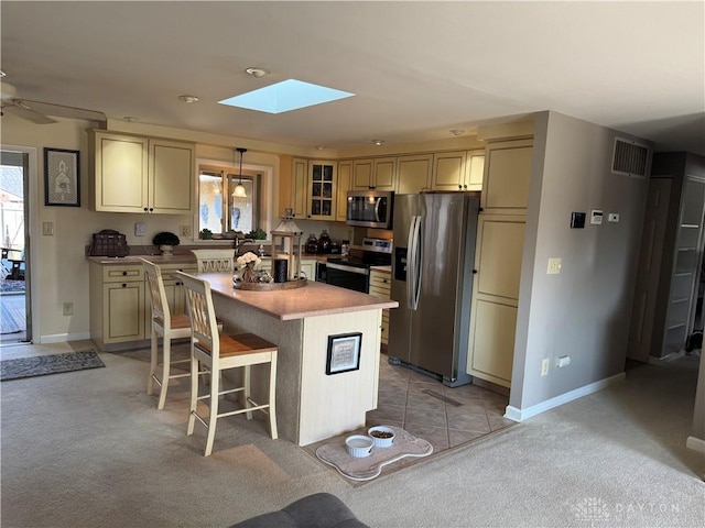 kitchen with a kitchen bar, cream cabinetry, a kitchen island, stainless steel appliances, and a skylight