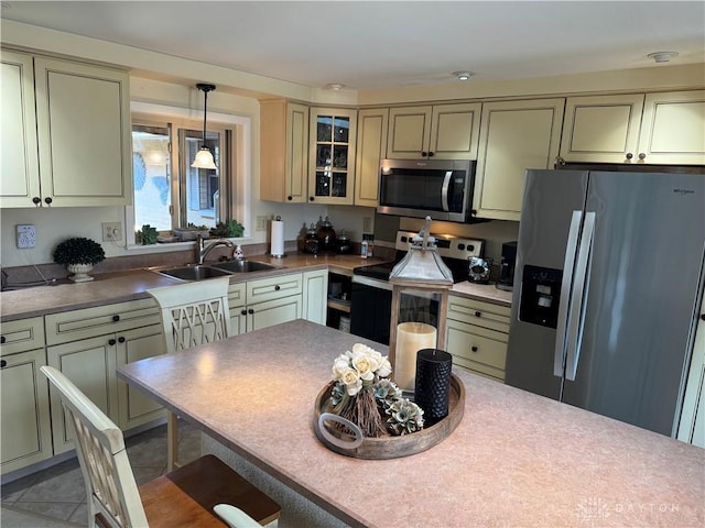 kitchen with hanging light fixtures, appliances with stainless steel finishes, cream cabinets, and a sink