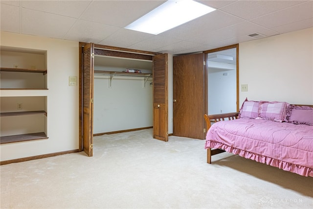 carpeted bedroom with a drop ceiling, a closet, baseboards, and visible vents