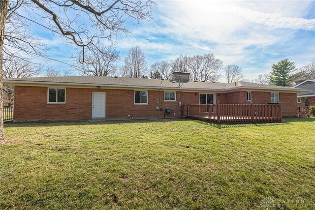 back of house with a wooden deck, a lawn, a chimney, and brick siding