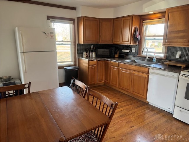 kitchen with white appliances, dark countertops, light wood-style floors, and a sink