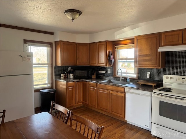 kitchen with dark wood-type flooring, a sink, dark countertops, white appliances, and brown cabinetry